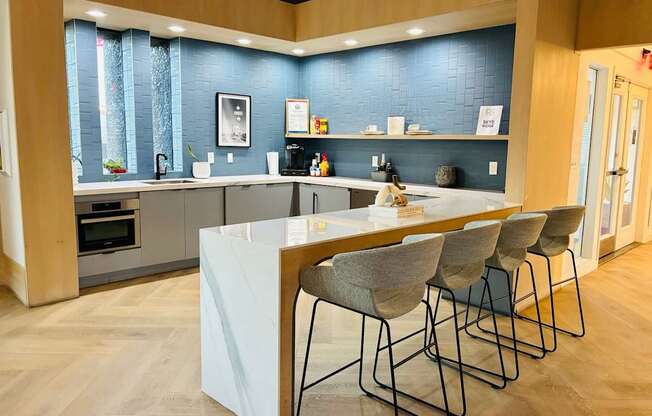 A modern kitchen with a white island and grey chairs.