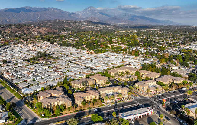A residential area with houses and streets in the foreground and mountains in the background.