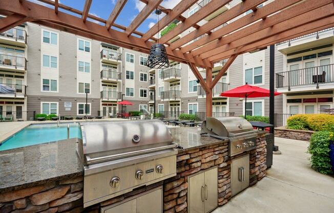 a patio with a grill and a pool with an apartment building at Link Apartments® Brookstown, Winston Salem, North Carolina