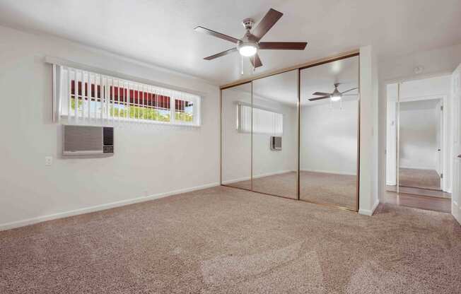 1 Bedroom Apartments In San Lorenzo, CA - Lorenzo Commons - Spacious Bedroom With Carpet Flooring, A Closet With Mirror Doors, A Ceiling Fan, A Window, And An A/C Unit