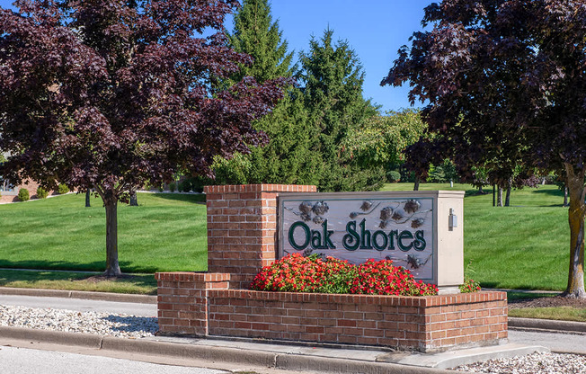An entrance sign with mature shade trees at Oak Shores Apartments in Oak Creek, WI