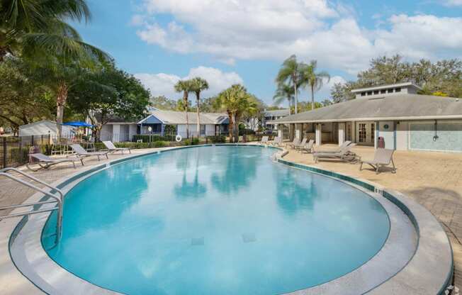 a large swimming pool with chairs and a house in the background at Aqua Bay Apartments in Naples, FL 34116