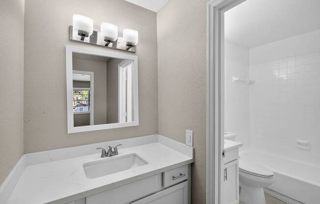 A white bathroom with a sink, mirror, and toilet.