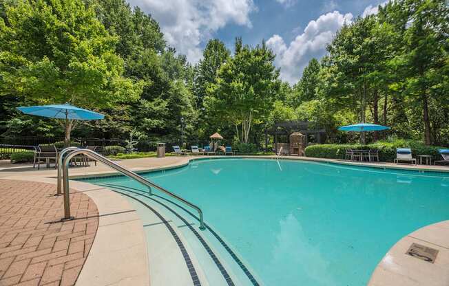 a swimming pool with trees in the background and blue umbrellas