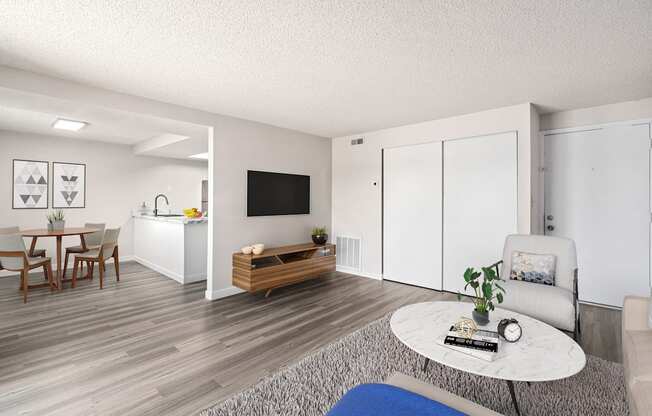 A living room with a white sofa, a grey coffee table, a wooden bench, and a dining table with chairs.