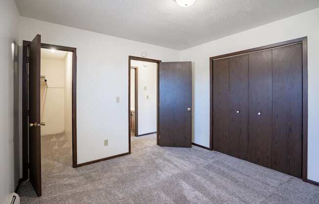 A room with a carpeted floor and three doors. West Fargo, ND Parkwest Gardens
