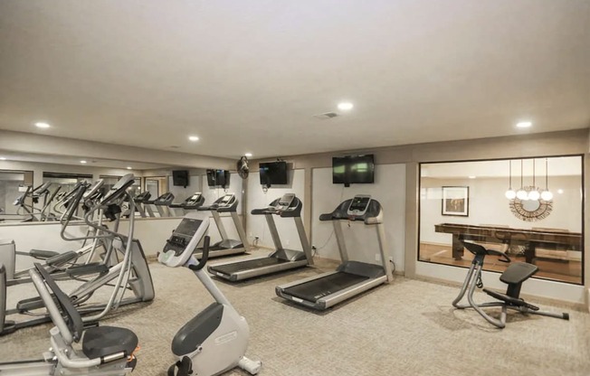 A spacious gym with treadmills, exercise bikes, and a television.