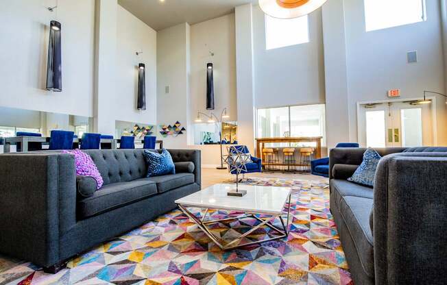 A large room with a grey couch and a colorful rug.