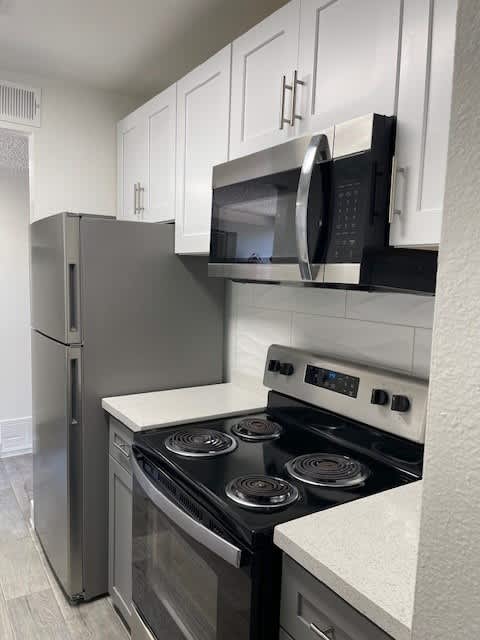 A kitchen with a stove, refrigerator, and microwave.