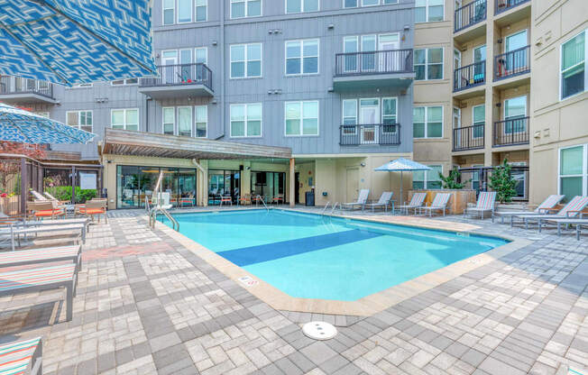 a swimming pool with lounge chairs and umbrellas in front of an apartment building