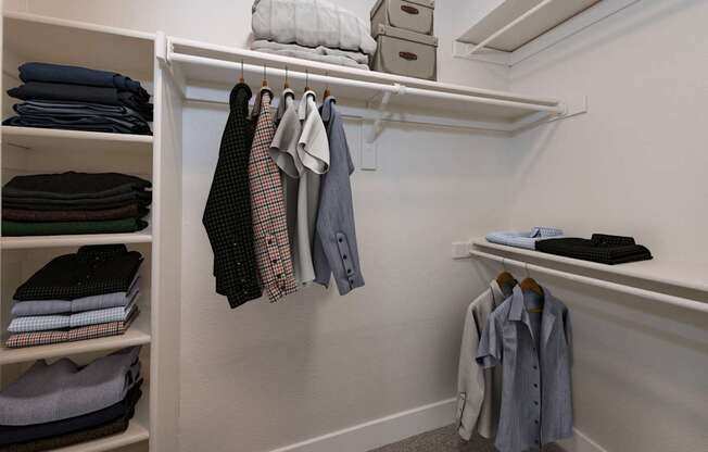 A white closet with clothes hanging and folded on shelves.