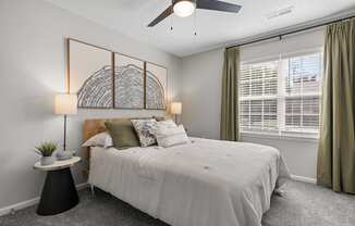 A bedroom with a large bed, a ceiling fan, and a wall art piece.