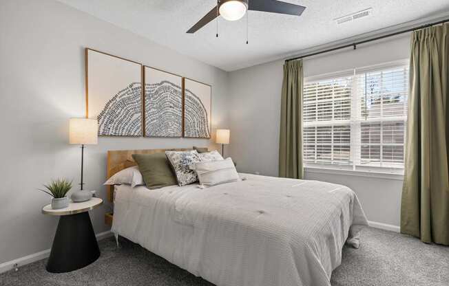 A bedroom with a large bed, a ceiling fan, and a wall art piece.