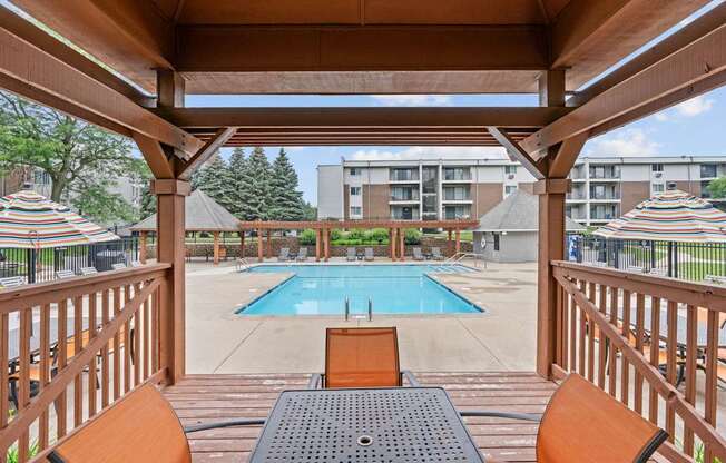 A wooden deck with a table and chairs overlooking a pool.