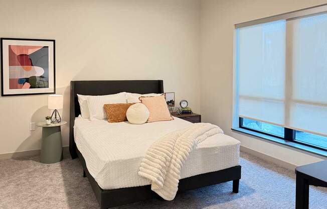 a bedroom with modern decor, a queen-sized bed, and a large window with a roller shade