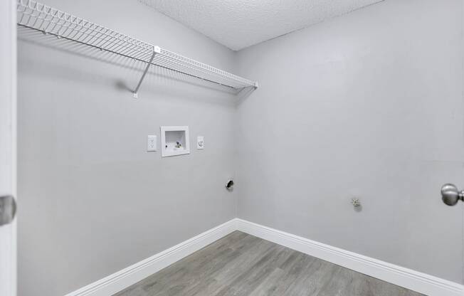 an empty room with white walls and wood flooring and a wire shelf on top