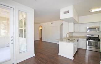 A kitchen with white cabinets and a wooden floor at The Kitt at Warner Center Apartments, Woodland Hills