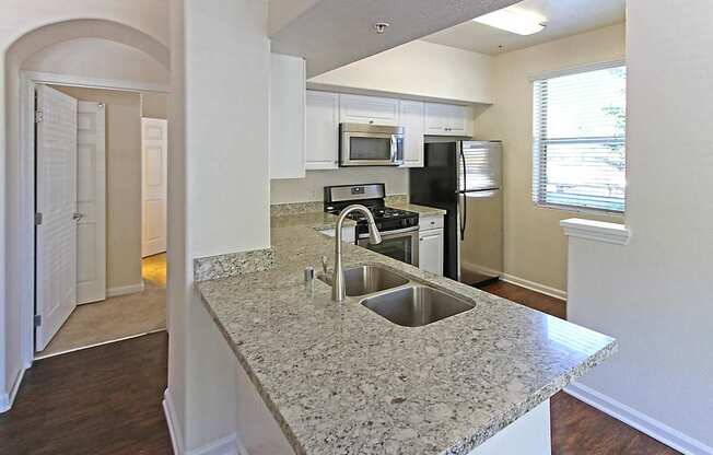 A kitchen with granite countertops and stainless steel appliances at The Kitt at Warner Center Apartments, Woodland Hills, California