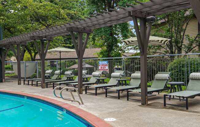 A pool with a wooden pergola and lounge chairs.