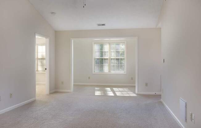 A large, empty room with a window and carpeted floor.