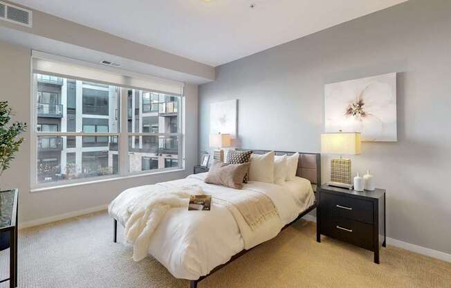 A bedroom with a large bed, a nightstand, and a window overlooking a building.
