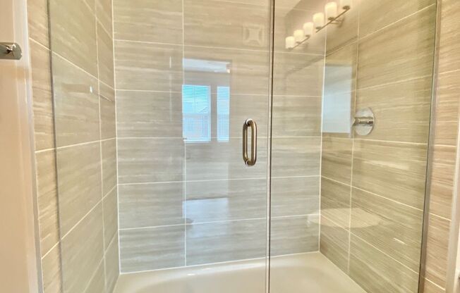 A large walk-in shower with glass doors and and modern floor-to-ceiling tile walls.