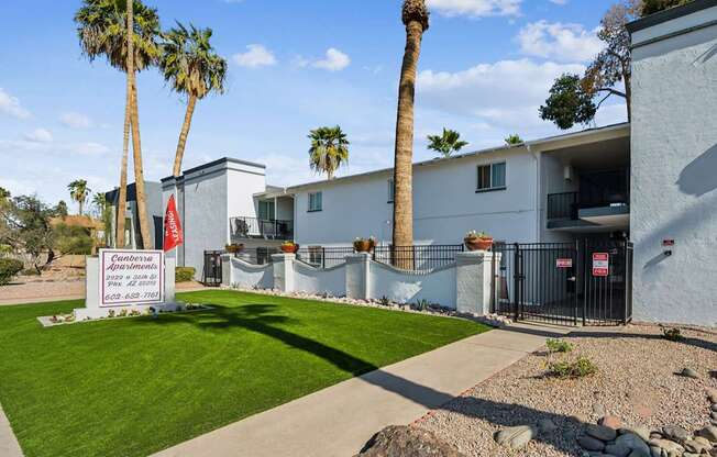 A sign for a condominium complex is in front of a white building with a black fence.