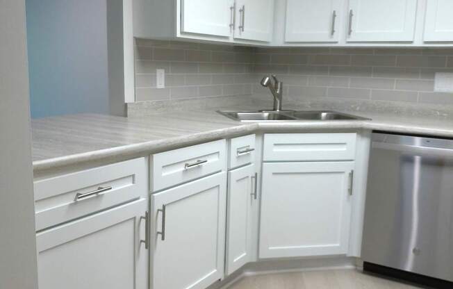 A kitchen with white cabinets and a stainless steel dishwasher.