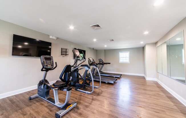 Fitness center at Ashton Brook Apartments features cardio equipment, televisions, and a large mirror