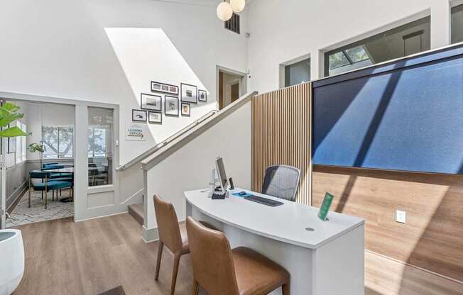 A room with a desk and chairs with a staircase in the background.