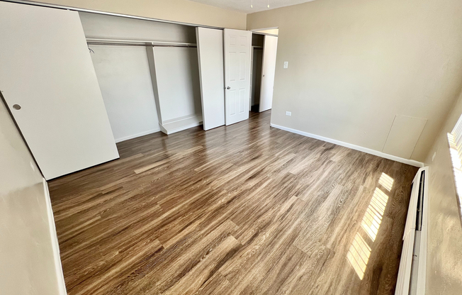 Bright and spacious bedroom with elegant wood flooring and abundant closet space, featuring a ceiling fan for comfort.