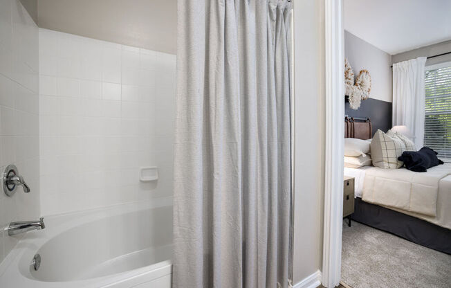 a bathroom with a bathtub and a bedroom in the background