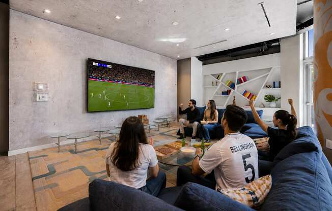 A group of people are watching a soccer game on a large TV screen in a modern living room.
