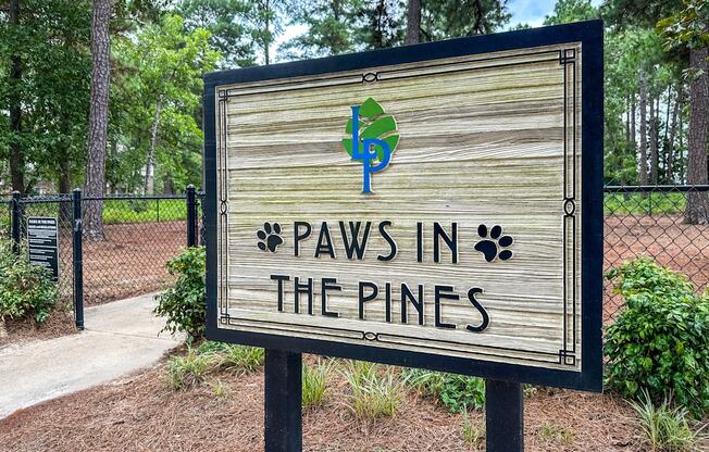 A wooden sign that says "Paws in the Pines" is in front of a fence.