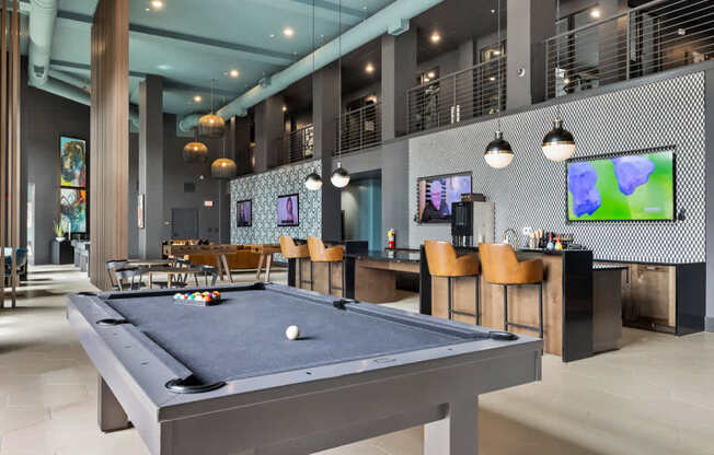 A pool table is in the middle of a room with a bar and television.
