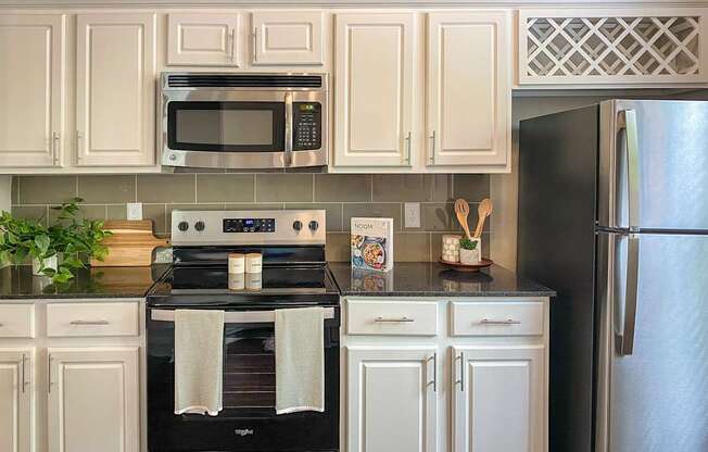 A kitchen with a black granite counter top and white cabinets in the 1486 square foot 3 bedroom, 3 bath apartment with attached 2-car garage at The Brownstones in Far North, Dallas, Texas