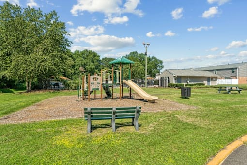 A playground with a green slide and two benches at Staples Mill Townhomes Apartments, Richmond 23228