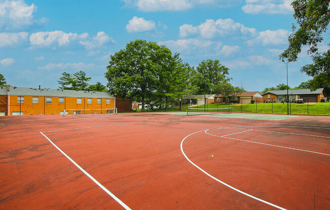 a red basketball court with trees and a building in the background
