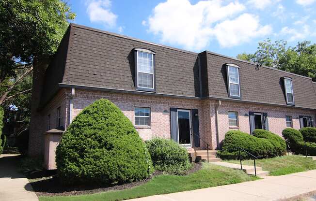 A house with a brown roof and a green bush in front.