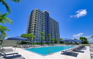 a large swimming pool with chaise lounge chairs and umbrellas in front of a tall at Regatta at New River, Florida, 33301