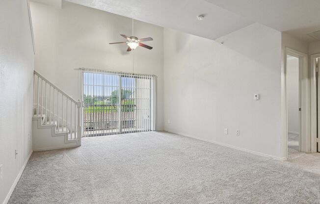 A room with a ceiling fan and a window with a view of a fence and trees.