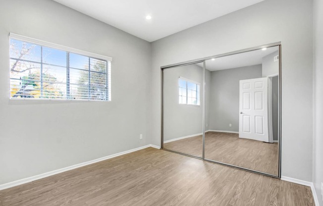 an empty bedroom with a mirrored closet door and a window