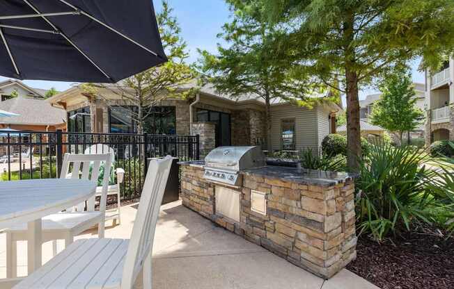 A patio with a grill and chairs under a black umbrella.