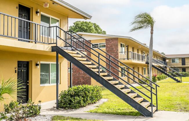 a yellow apartment building with stairs and a palm tree