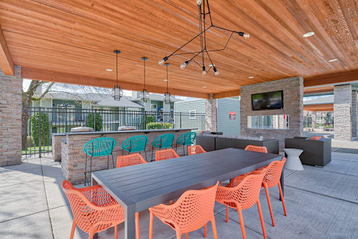 A long table with orange chairs is set up under a wooden roof.