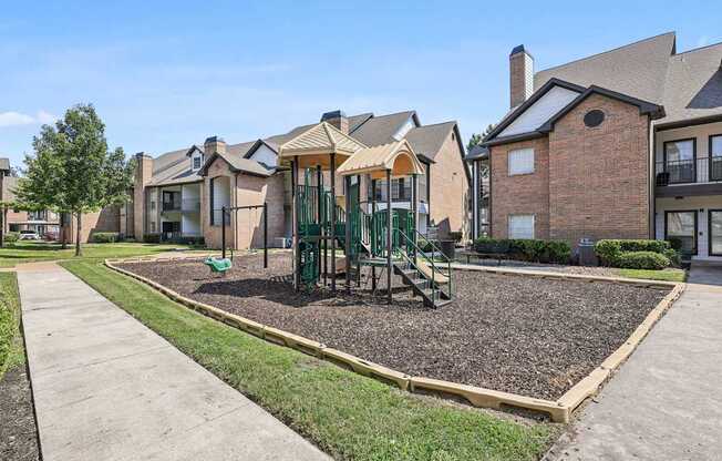 A playground with a green slide and a brown gravel area in front of a row of houses.