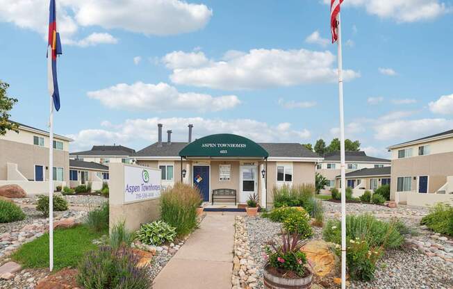 A building with a sign that says "Aspen Towers" is surrounded by flags and plants.