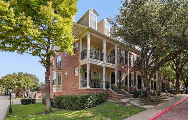 A red brick house with a balcony and a tree in front.