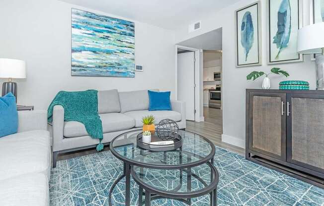 A living room with a grey couch and a glass coffee table.