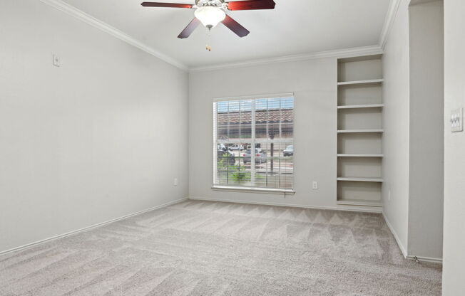 A room with a ceiling fan and a window overlooking a parking lot.